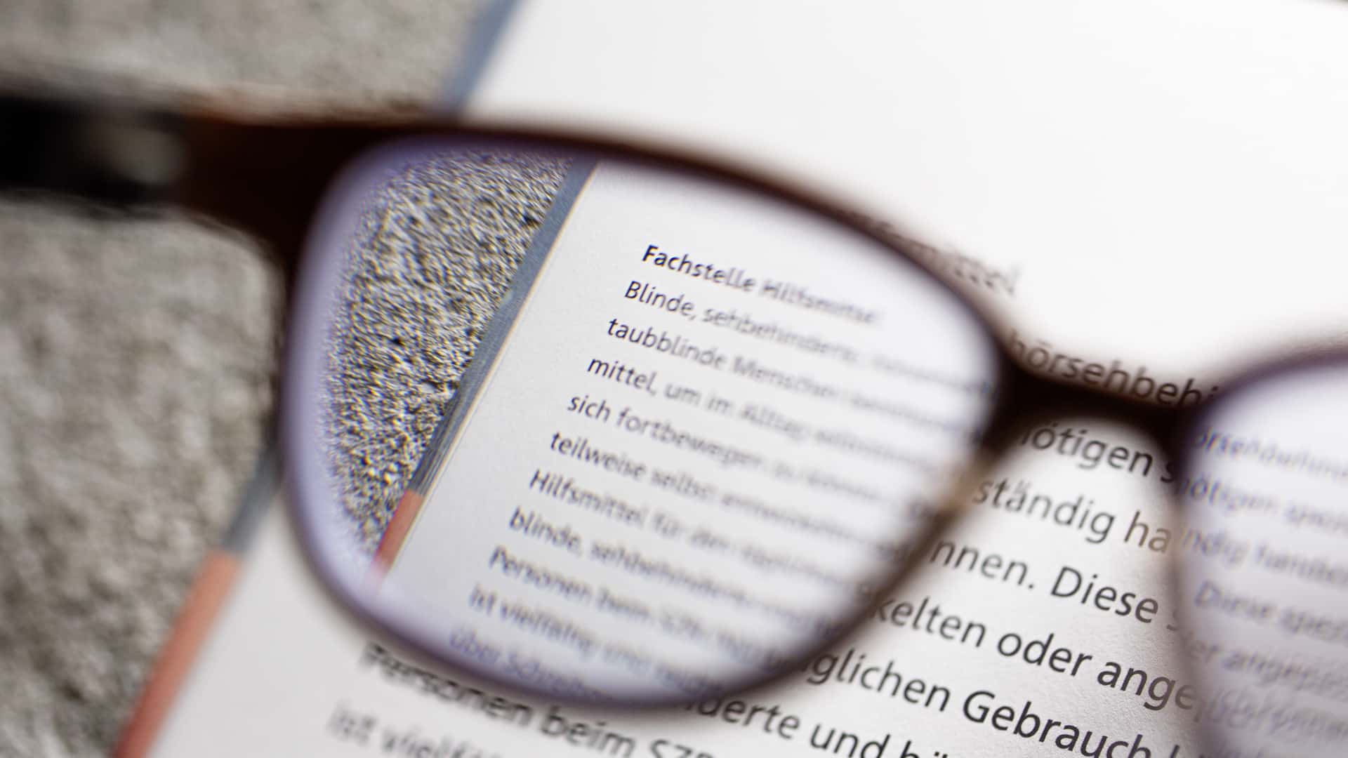 Text fokussiert durch Brille Brille liegt auf einem Buch, der Text ist durch das Glas vergrössert sichtbar.
